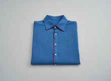Load image into Gallery viewer, Folded blue shirt with red trim on a gray background