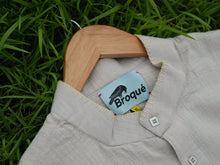 Load image into Gallery viewer, broque beige shirt with a wooden hanger on grass, featuring a Broqué label.