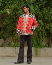 Load image into Gallery viewer, Man wearing a red and black patterned shirt with black pants standing in front of green foliage.