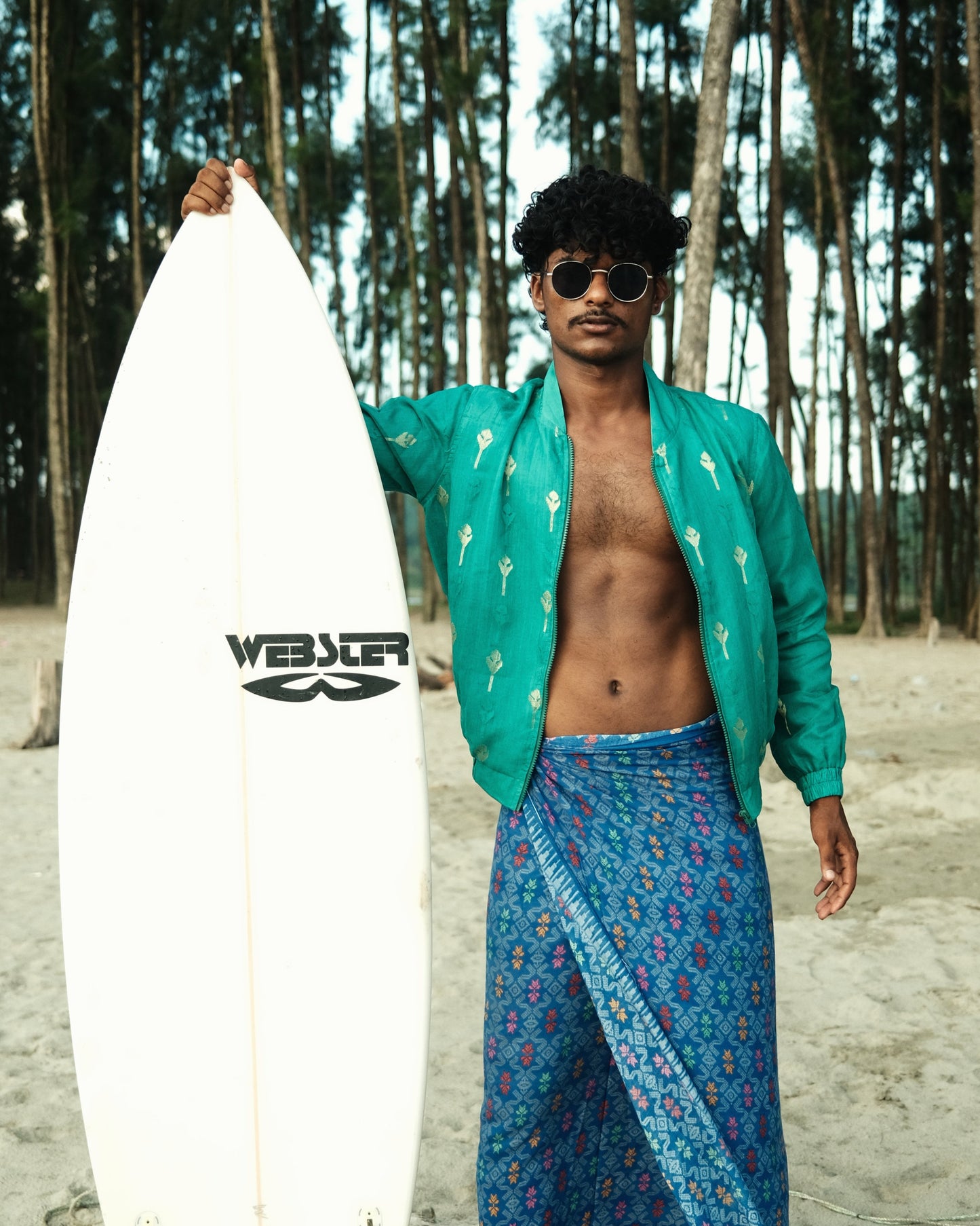 Man holding a surfboard with a brand logo on a beach