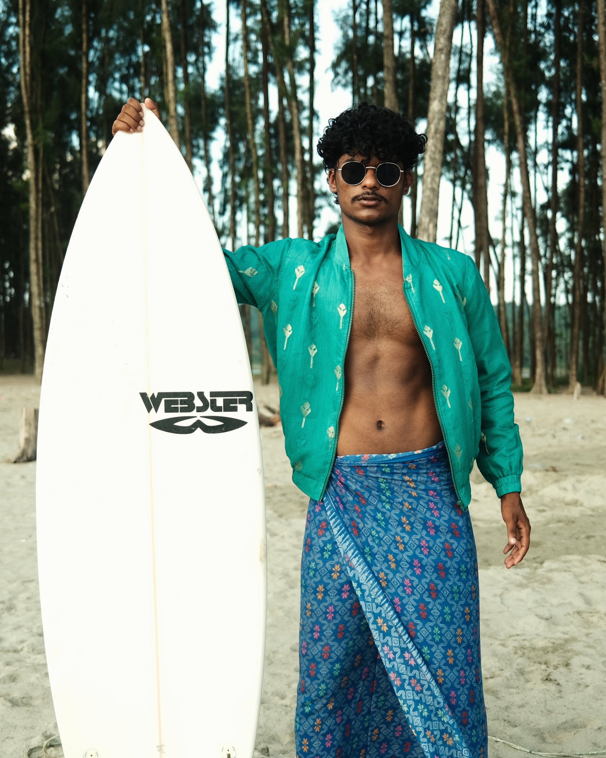 Man holding a surfboard with a brand logo on a beach