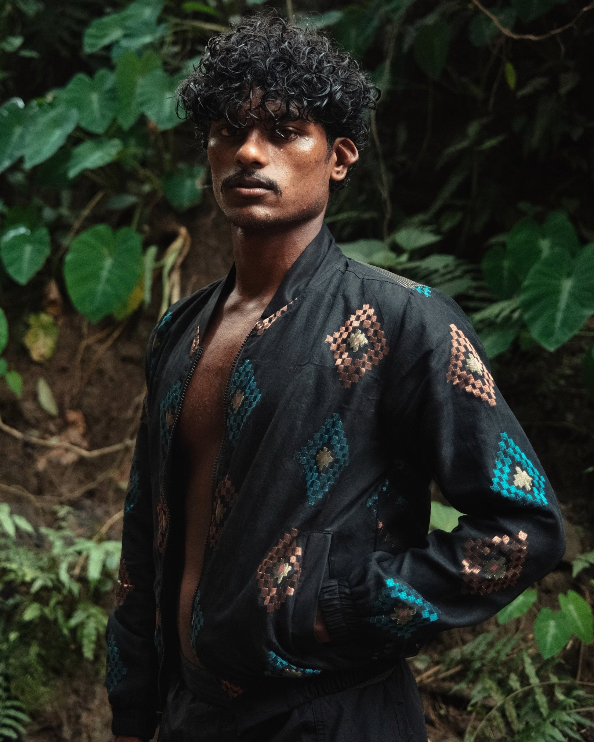 Man wearing a black embroidered jacket in a forest setting