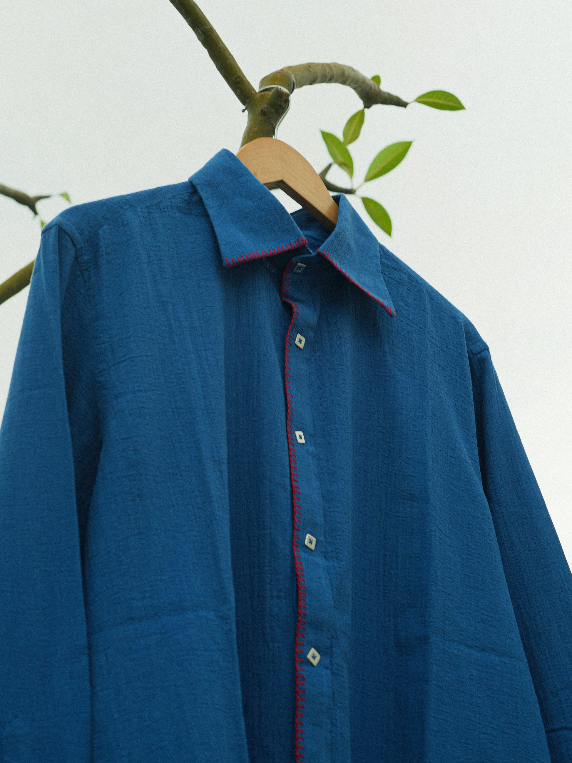 Blue shirt with red accents on a hanger against a white background