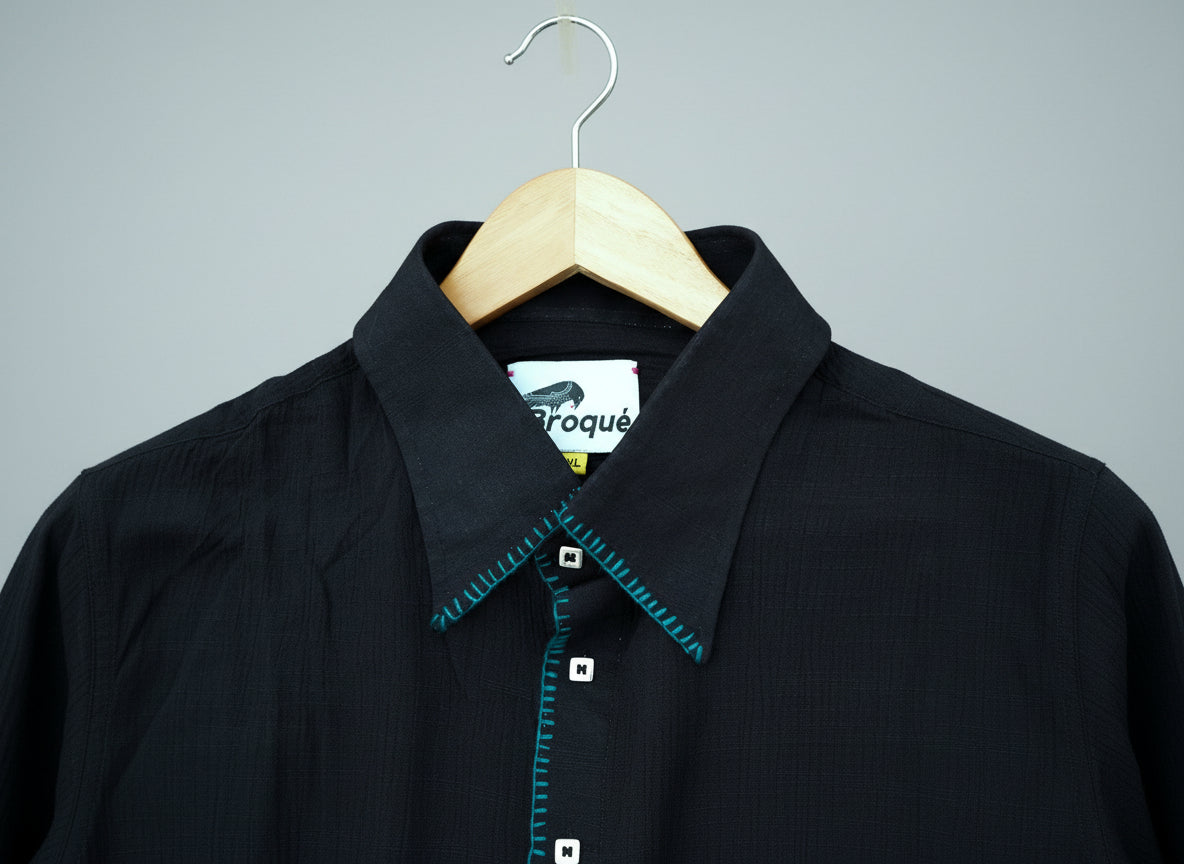 Black shirt with teal stitching on a wooden hanger against a grass background