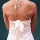 Back view of a person wearing a white dress with thin straps and a bow detail on a dark background