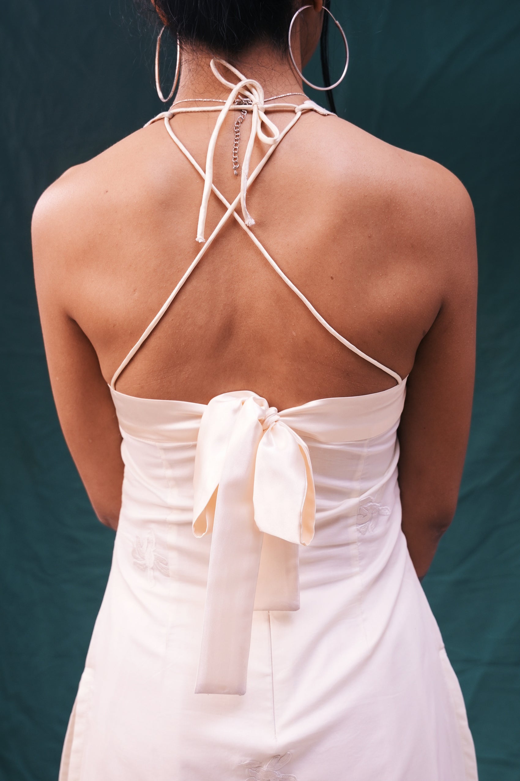 Back view of a person wearing a white dress with thin straps and a bow detail on a dark background