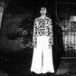 Black and white photo of a person standing on a reflective surface with a patterned coat.