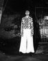 Black and white photo of a person standing on a reflective surface with a patterned coat.