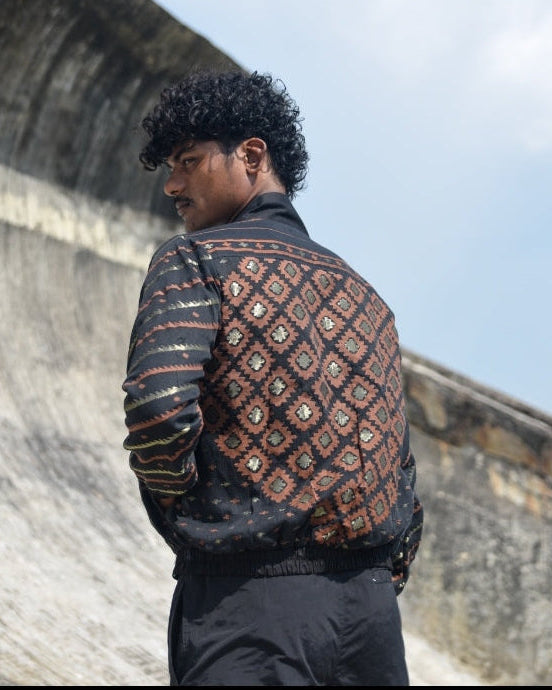 Person wearing a patterned jacket standing against a stone wall with a blue sky background