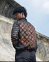 Person wearing a patterned jacket standing against a stone wall with a blue sky background