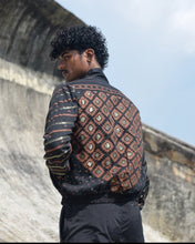 Load image into Gallery viewer, Person wearing a patterned jacket standing against a stone wall with a blue sky background

