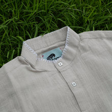 Load image into Gallery viewer, broque beige shirt with a brand label on a grass background
